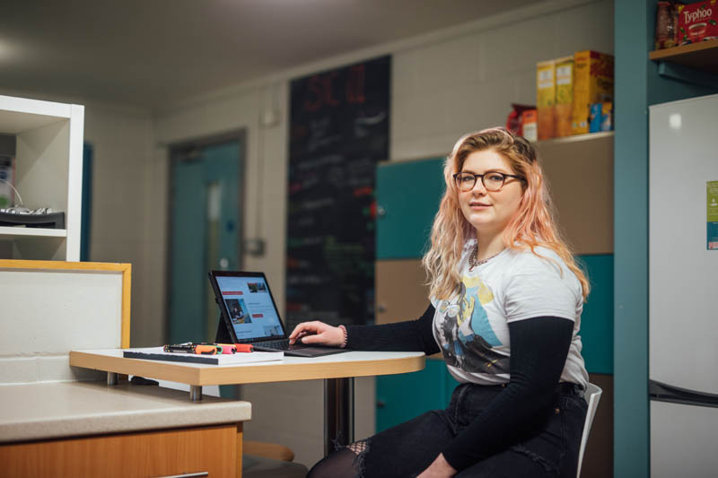 Image of Orla in Elms Ktichen sitting on a stool with laptop open