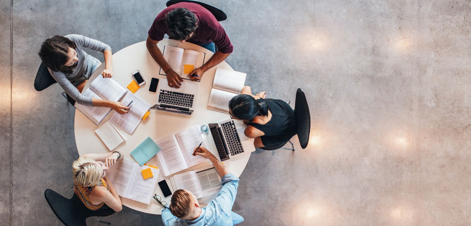 aerial view of mixed study group sitting at a round table with books, notepads, laptops, etc