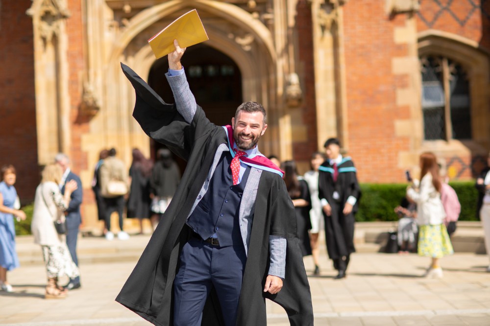 male graduate holding graduation programme or certificate up in the air