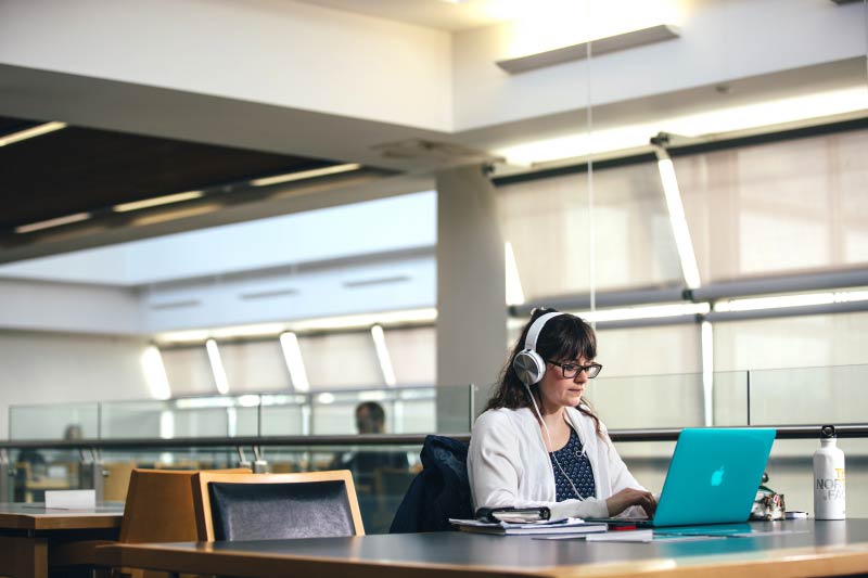 female student wearing headphones and using blue laptop in the McClay library