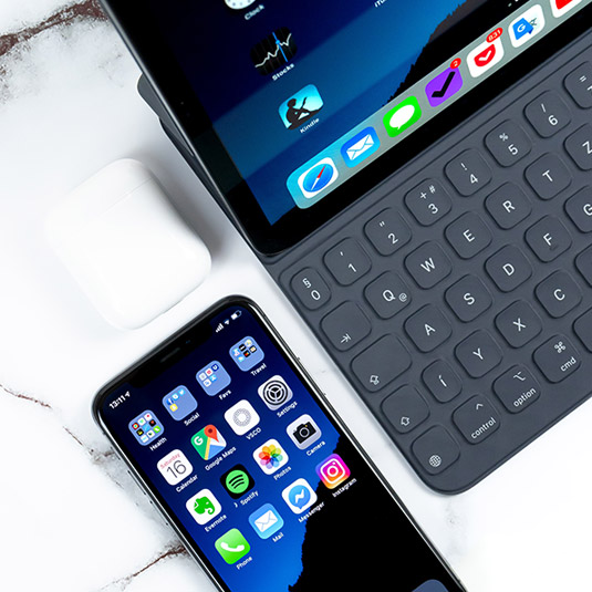 An open laptop  on a desk with a smartphone placed beside it.